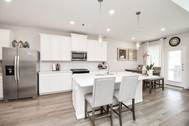 kitchen with sink, hanging light fixtures, light hardwood / wood-style flooring, a kitchen island with sink, and appliances with stainless steel finishes