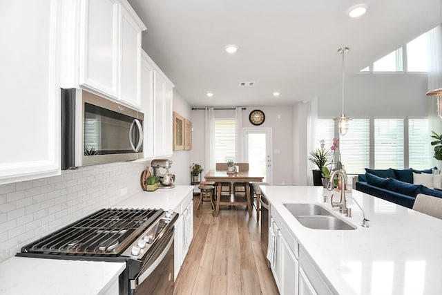 kitchen with sink, light hardwood / wood-style flooring, appliances with stainless steel finishes, decorative light fixtures, and white cabinetry