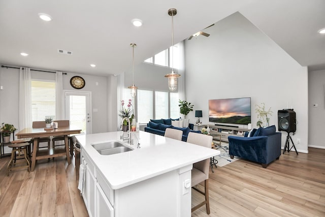 kitchen with a kitchen island with sink, sink, pendant lighting, and light wood-type flooring