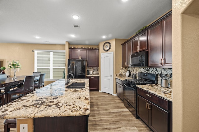 kitchen with backsplash, black appliances, sink, an island with sink, and light hardwood / wood-style floors