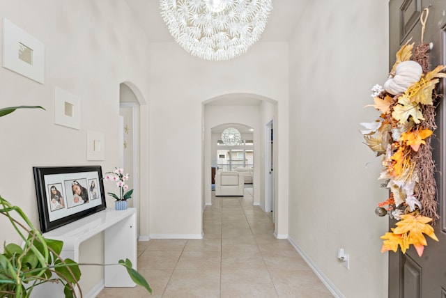 hall featuring a towering ceiling, an inviting chandelier, and light tile patterned floors