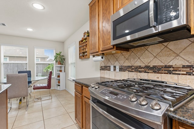 kitchen with light tile patterned floors, dark stone countertops, backsplash, and appliances with stainless steel finishes