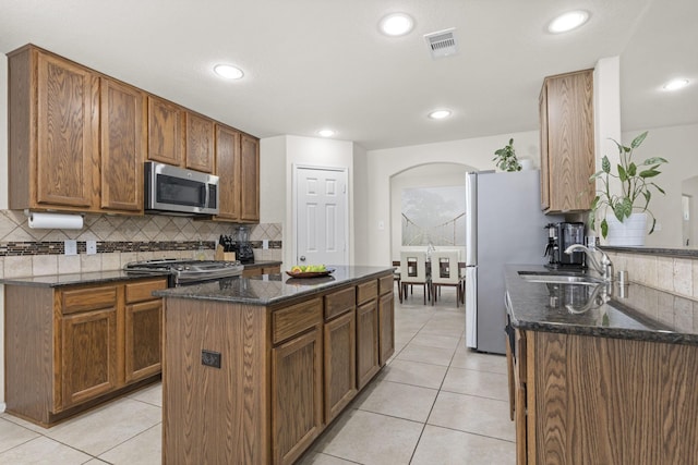 kitchen featuring light tile patterned floors, a kitchen island, backsplash, appliances with stainless steel finishes, and sink