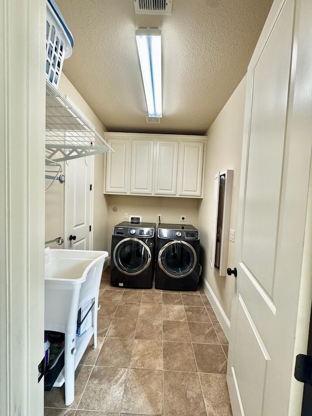 laundry area featuring cabinets, a textured ceiling, and washing machine and clothes dryer