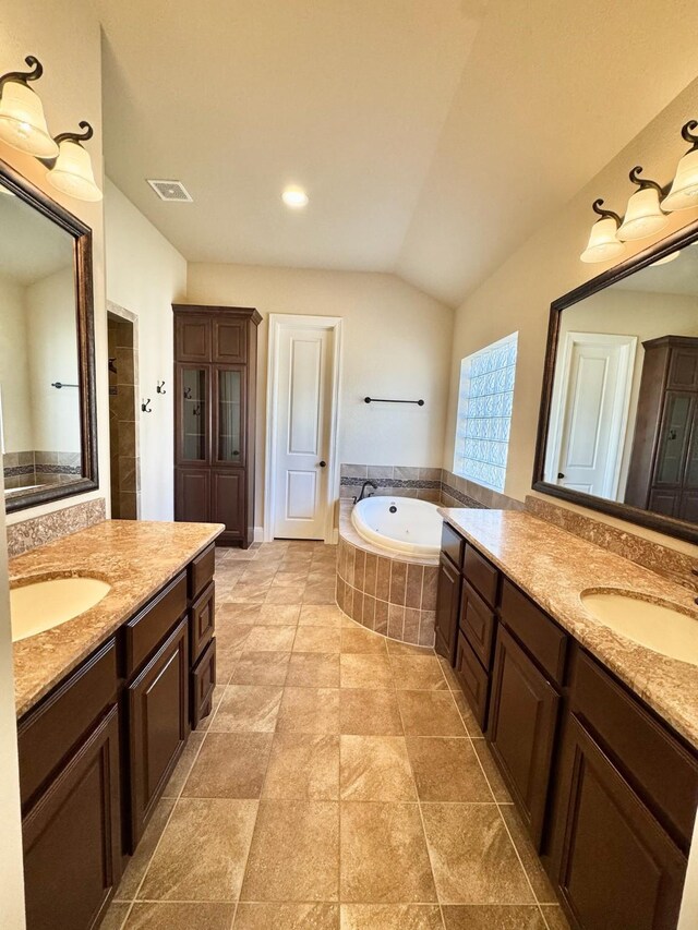 bathroom with vanity, vaulted ceiling, and tiled tub