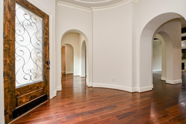 foyer entrance featuring arched walkways, ornamental molding, dark wood-style flooring, and baseboards