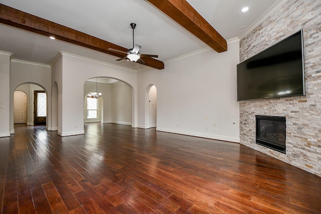 unfurnished living room with ceiling fan with notable chandelier, dark wood-type flooring, a fireplace, baseboards, and beamed ceiling