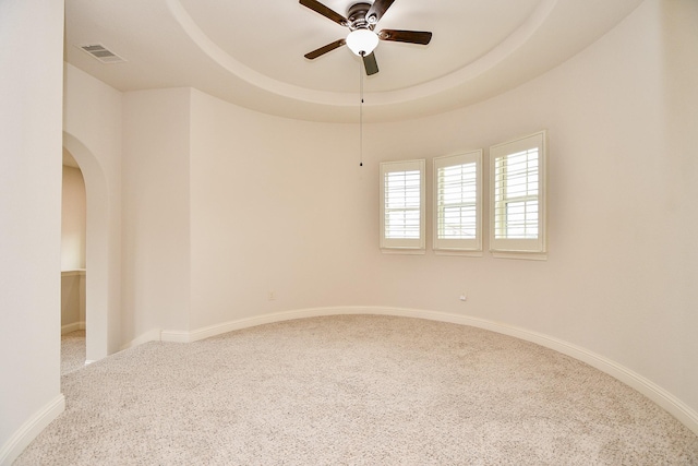 unfurnished room featuring arched walkways, visible vents, baseboards, a ceiling fan, and a tray ceiling