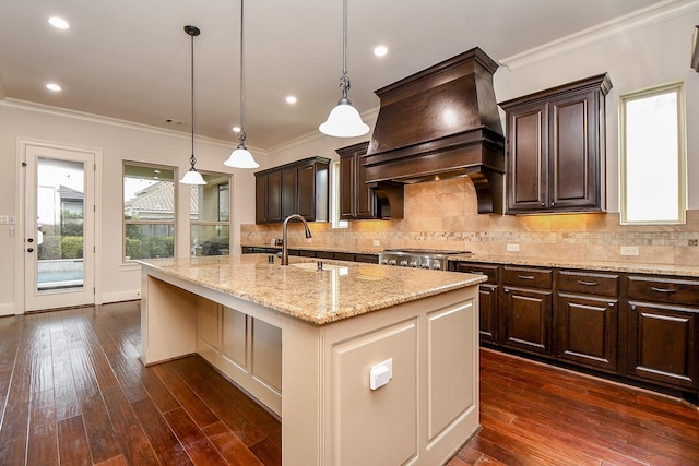 kitchen featuring a center island with sink, dark wood-style floors, decorative light fixtures, premium range hood, and a sink