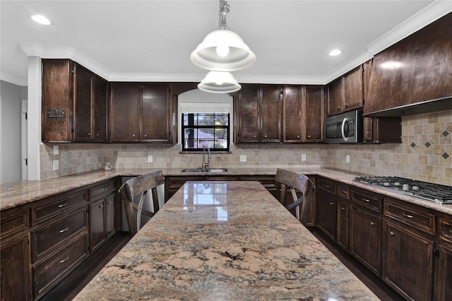 kitchen with light stone counters, dark brown cabinetry, stainless steel appliances, sink, and hanging light fixtures