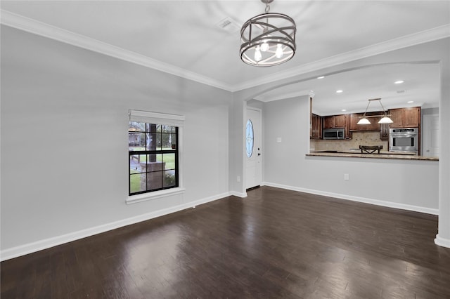 unfurnished living room with dark hardwood / wood-style floors, crown molding, and an inviting chandelier