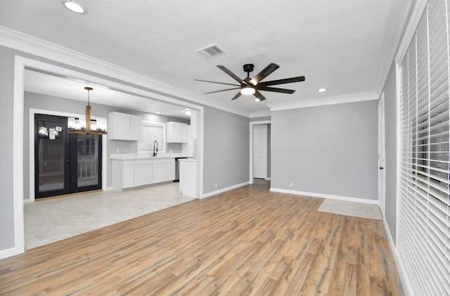 unfurnished living room with ceiling fan with notable chandelier, light hardwood / wood-style floors, and ornamental molding