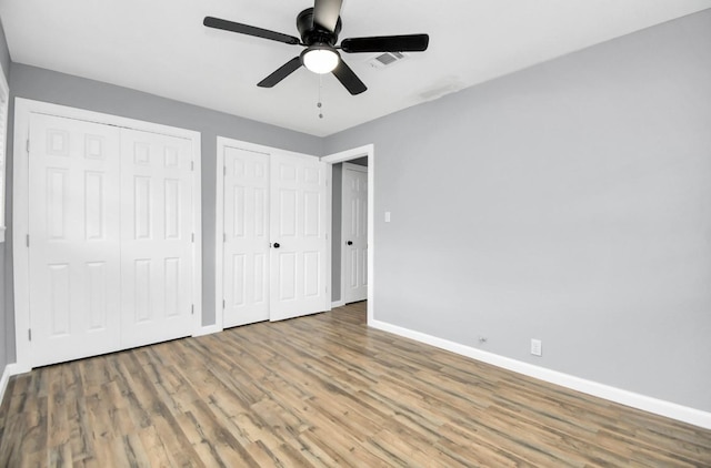 unfurnished bedroom featuring ceiling fan, wood-type flooring, and two closets