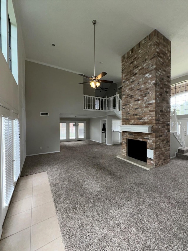 unfurnished living room with a large fireplace, a wealth of natural light, ceiling fan, and a high ceiling