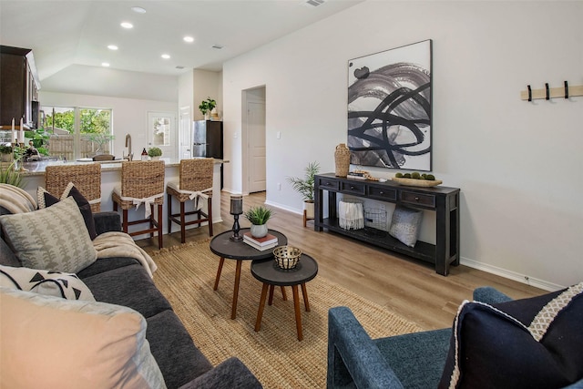 living room featuring light hardwood / wood-style floors, lofted ceiling, and sink