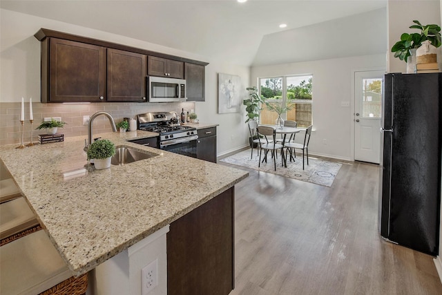 kitchen featuring lofted ceiling, light stone countertops, stainless steel appliances, and kitchen peninsula