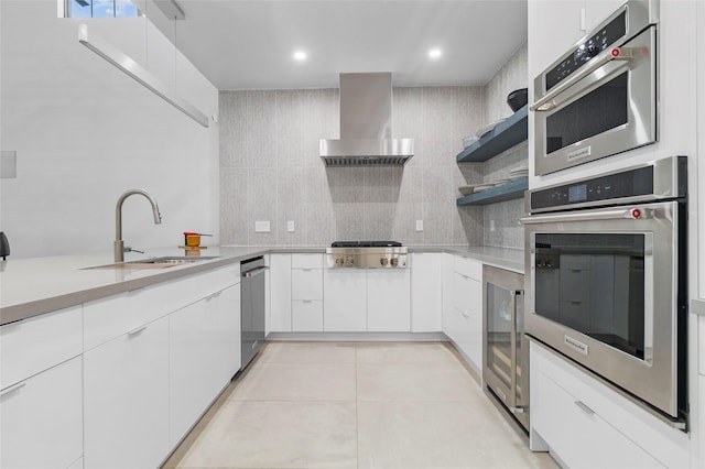 kitchen with appliances with stainless steel finishes, sink, wall chimney range hood, white cabinetry, and light tile patterned flooring