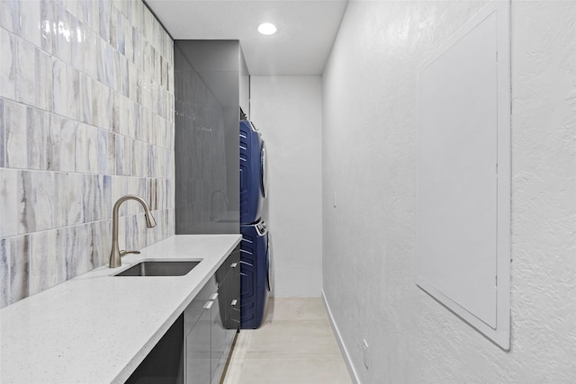 clothes washing area featuring light tile patterned floors, sink, tile walls, and stacked washer / drying machine