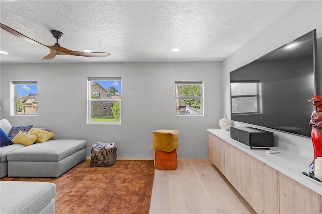 living room featuring ceiling fan, a textured ceiling, and light wood-type flooring