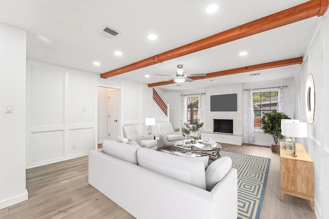 living room featuring ceiling fan, a large fireplace, beamed ceiling, and light wood-type flooring