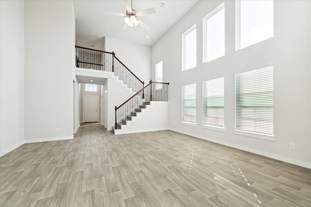 unfurnished living room featuring ceiling fan, light hardwood / wood-style flooring, and a high ceiling