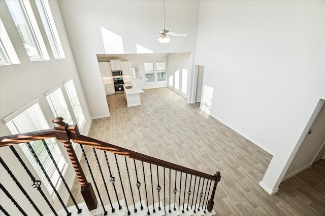 staircase with ceiling fan, hardwood / wood-style floors, and a high ceiling