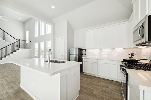 kitchen with appliances with stainless steel finishes, sink, white cabinets, hardwood / wood-style floors, and an island with sink