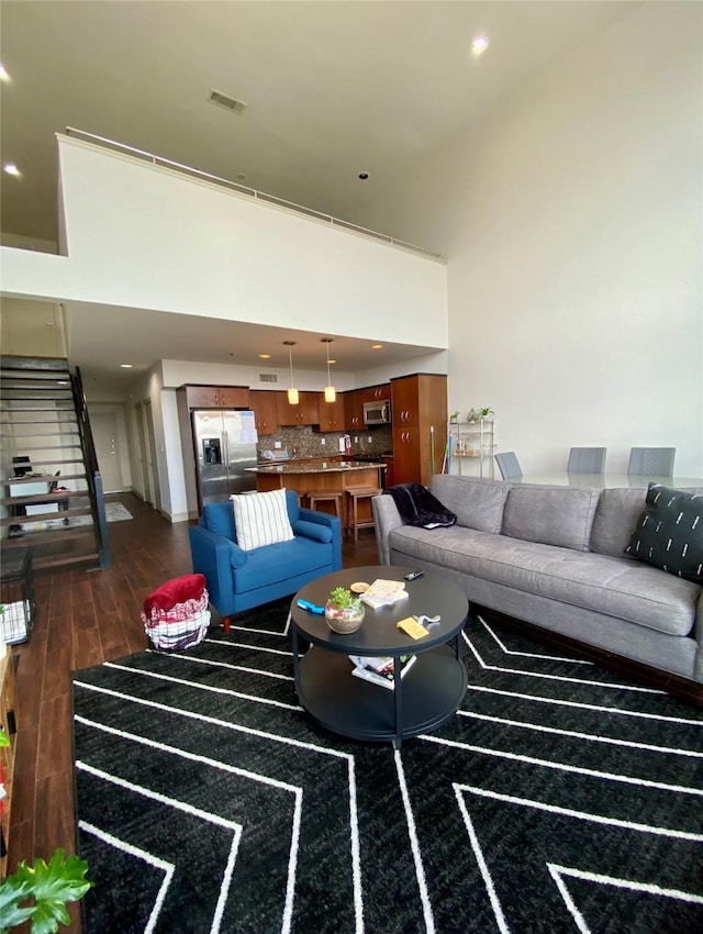 living area with recessed lighting, a high ceiling, visible vents, stairway, and dark wood-style floors