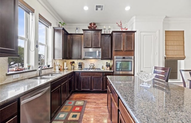 kitchen with light stone countertops, sink, light wood-type flooring, appliances with stainless steel finishes, and ornamental molding