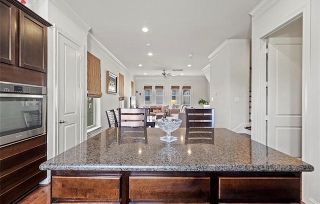 kitchen featuring dark brown cabinets, crown molding, stone countertops, a center island, and oven