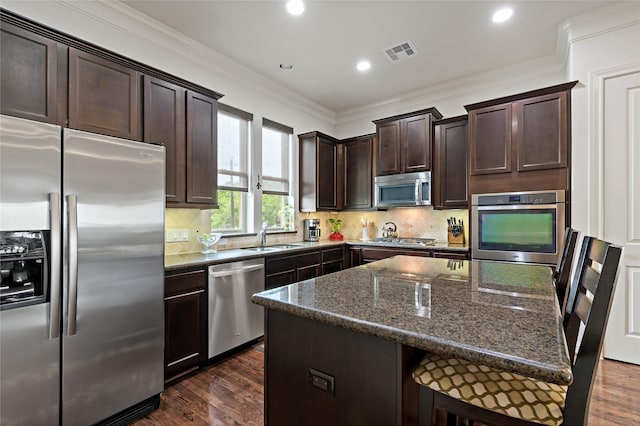 kitchen featuring dark hardwood / wood-style floors, a center island, appliances with stainless steel finishes, and dark stone counters