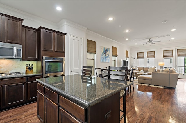 kitchen with stainless steel appliances, dark hardwood / wood-style flooring, dark stone countertops, a kitchen island, and ornamental molding