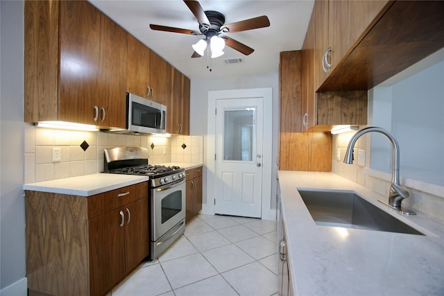 kitchen featuring ceiling fan, sink, backsplash, light tile patterned floors, and appliances with stainless steel finishes