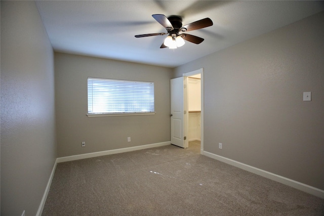 unfurnished bedroom featuring a walk in closet, light colored carpet, and ceiling fan