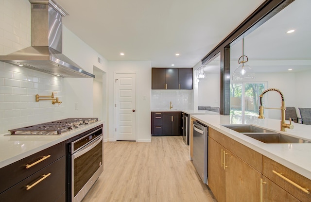 kitchen with pendant lighting, light hardwood / wood-style flooring, wall chimney exhaust hood, decorative backsplash, and appliances with stainless steel finishes