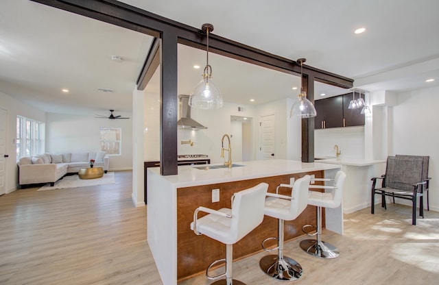 kitchen featuring a kitchen breakfast bar, wall chimney range hood, sink, hanging light fixtures, and light hardwood / wood-style floors