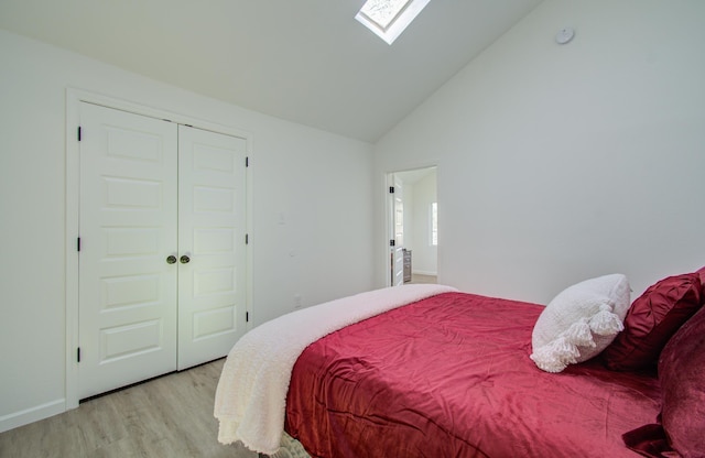 bedroom featuring a skylight, a closet, high vaulted ceiling, and light wood-type flooring