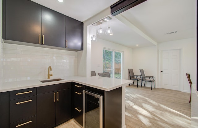 kitchen with kitchen peninsula, tasteful backsplash, beverage cooler, decorative light fixtures, and light hardwood / wood-style floors