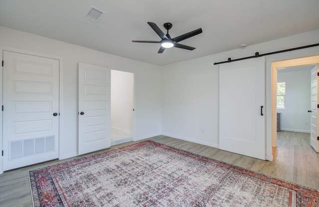 unfurnished bedroom featuring a barn door, light hardwood / wood-style flooring, and ceiling fan