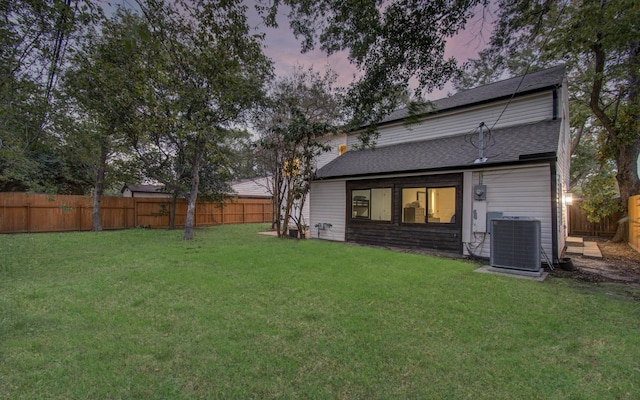 back house at dusk featuring central AC unit and a lawn