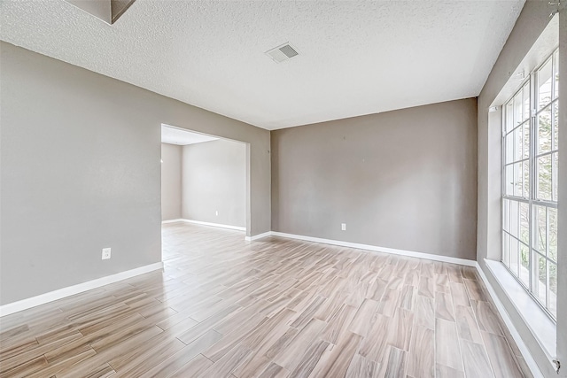 unfurnished room with light hardwood / wood-style floors, a textured ceiling, and a wealth of natural light