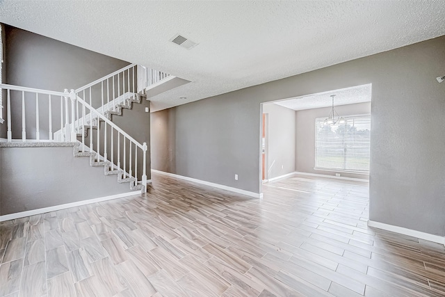 unfurnished living room featuring hardwood / wood-style floors, a textured ceiling, and an inviting chandelier