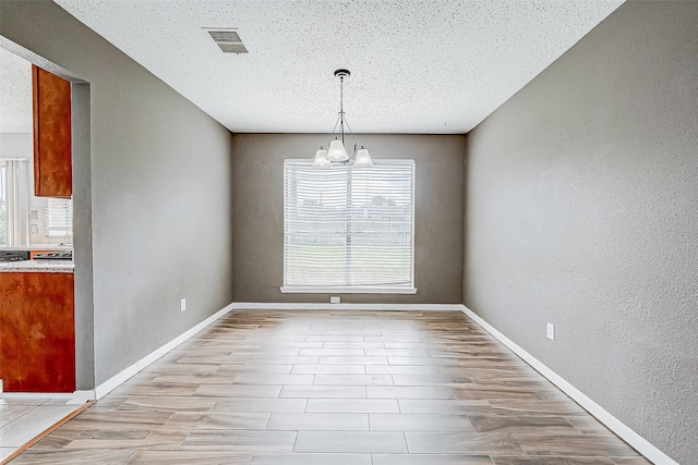 unfurnished dining area featuring light hardwood / wood-style flooring, a textured ceiling, and a notable chandelier