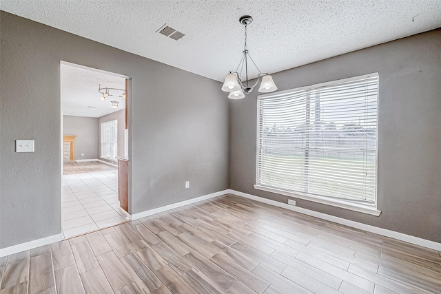 spare room featuring a notable chandelier, light wood-type flooring, and a textured ceiling