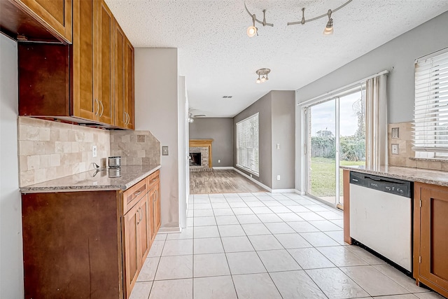 kitchen featuring dishwasher, light tile patterned floors, a textured ceiling, a fireplace, and light stone counters