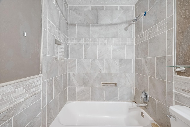 bathroom with a textured ceiling, toilet, tiled shower / bath, and tile walls