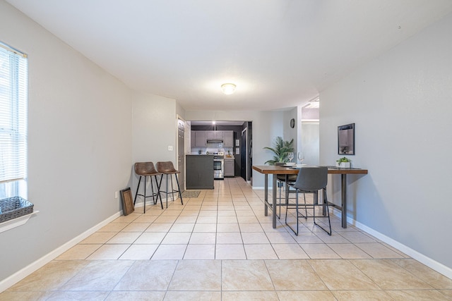 kitchen with a breakfast bar area, kitchen peninsula, light tile patterned floors, and stainless steel range with electric stovetop