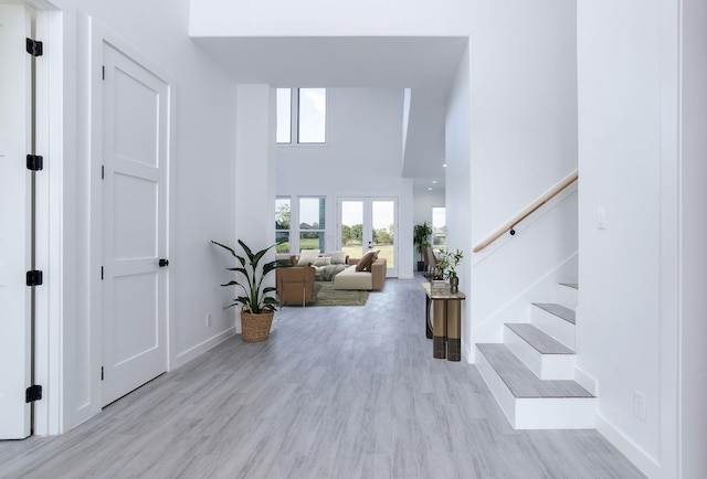 foyer entrance with french doors, light hardwood / wood-style floors, and a high ceiling