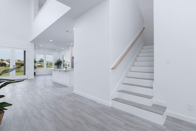 stairs with hardwood / wood-style floors, a towering ceiling, french doors, and sink