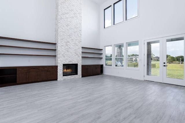 unfurnished living room with a fireplace, a high ceiling, light hardwood / wood-style floors, and french doors